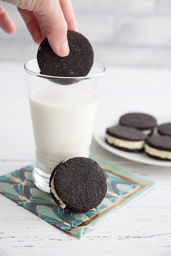 A hand dipping a keto oreo cookie into a glass of milk