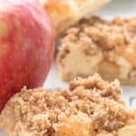 Close up shot of Keto Caramel Apple Cheesecake Bars on a white table with an apple beside them.