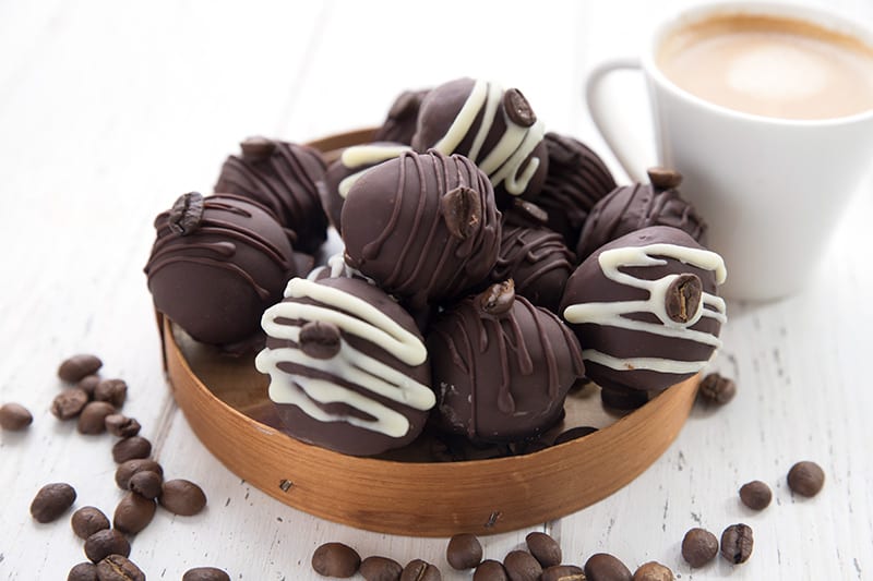 Keto chocolate truffles on a wooden plate with coffee beans around and a cup of espresso in the background.