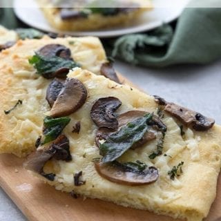 Titled image of keto flatbread with mushrooms and age on a wooden cutting board.