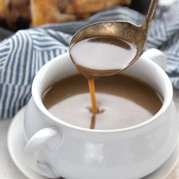 A ladle drizzling keto gravy into a white bowl.