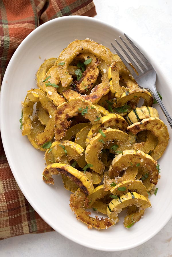 Top down photo of roasted delicata squash in a serving dish over a plaid napkin