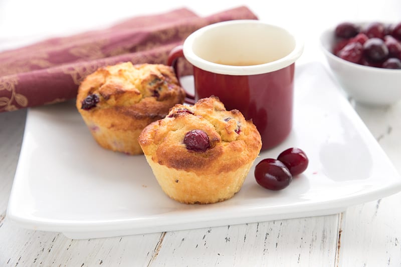 A white plate with two air fryer cranberry muffins and a red cup of coffee