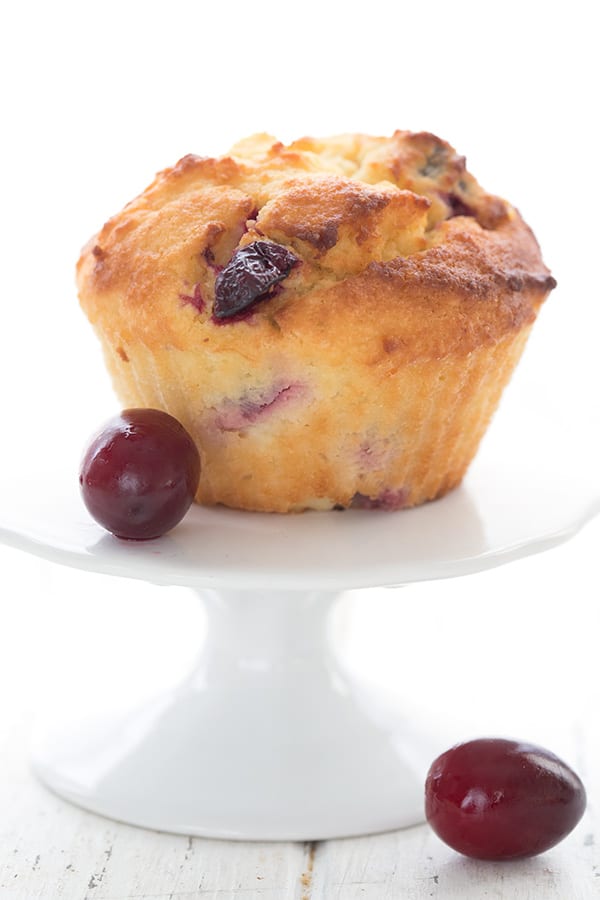 A keto cranberry orange muffin on a white cupcake stand with two fresh cranberries.