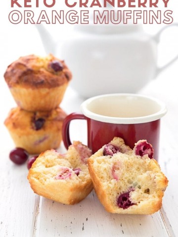 Titled image of keto cranberry orange muffins on a white table with a red cup of coffee. The muffin in front is broken up to show the inside.