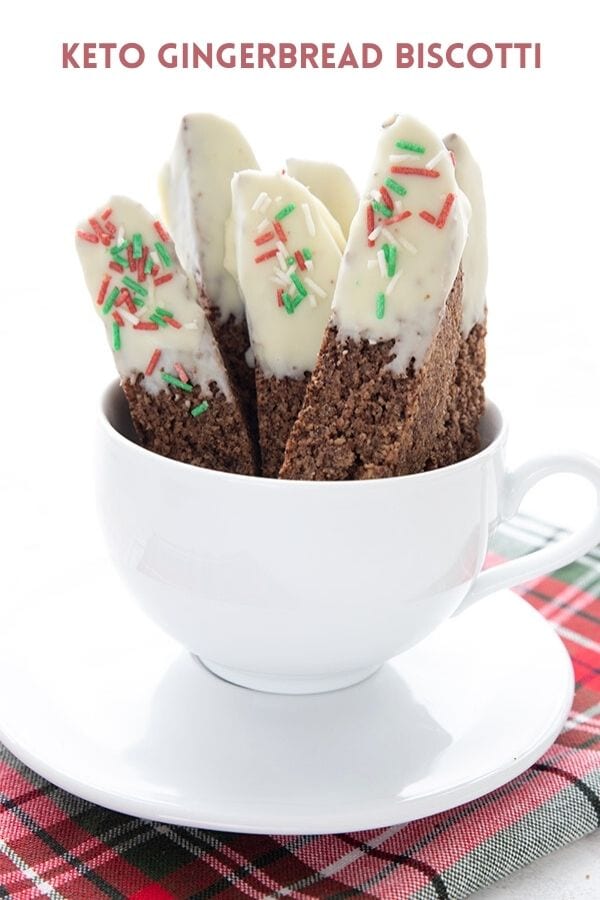 Titled image: A white coffee cup filled with keto gingerbread biscotti over a plaid green and red napkin.