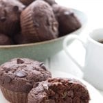 A keto chocolate zucchini muffin cut open on a white plate, with a bowl of muffins in behind.