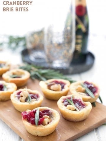 Titled image of Keto Cranberry Brie Bites on a wooden cutting board with champagne and glasses in the background.