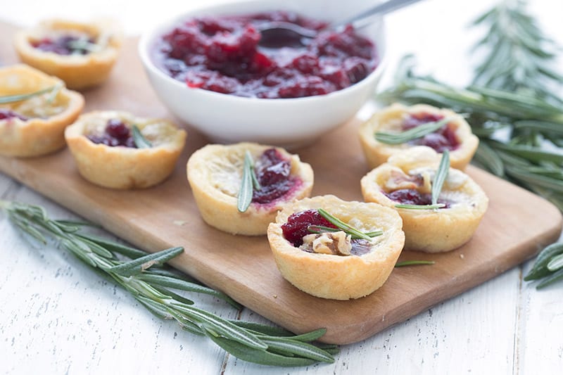 Keto cranberry brie bites on a wooden platter, surrounded by twigs of rosemary.