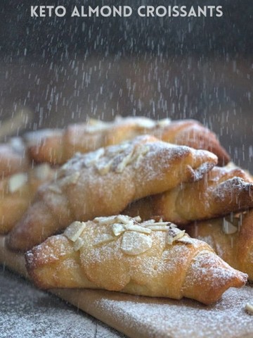 Titled image: A pile of keto almond croissants being sprinkled with powdered sweetener.