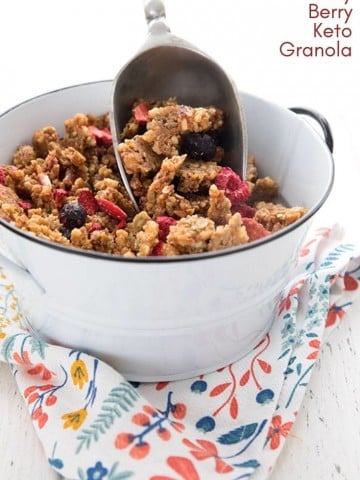 A white container full of keto granola over a patterned napkin, with a scoop in the container.