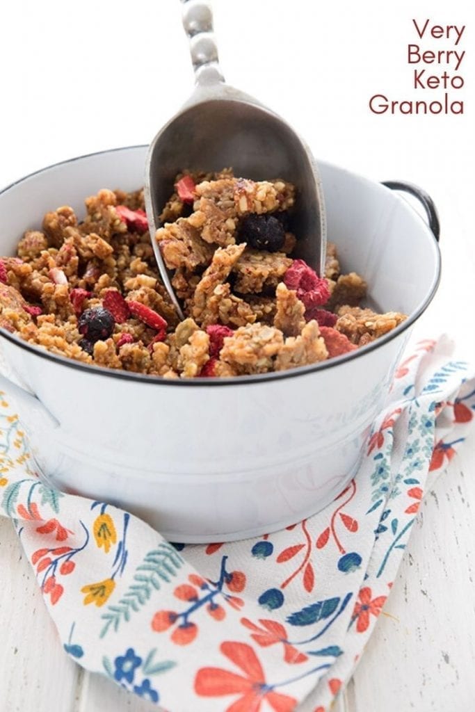 A white container full of keto granola over a patterned napkin, with a scoop in the container.
