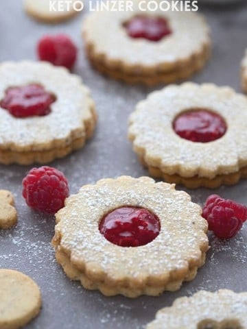 Titled image of keto Linzer cookies on a grey table with raspberries sprinkled around