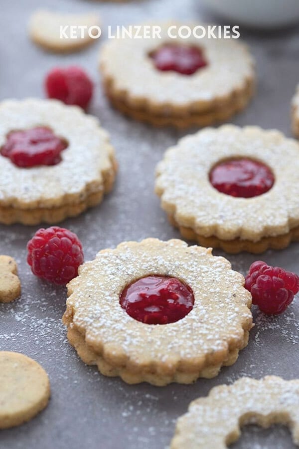 Titled image of keto Linzer cookies on a grey table with raspberries sprinkled around