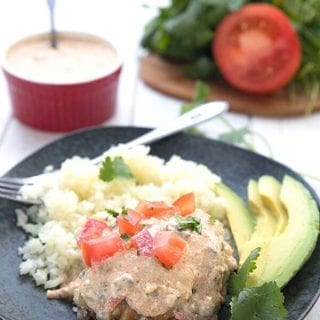 Titled image for Keto Slow Cooker Smothered Chicken, with a piece of chicken on a black plate with cauliflower rice and avocado.