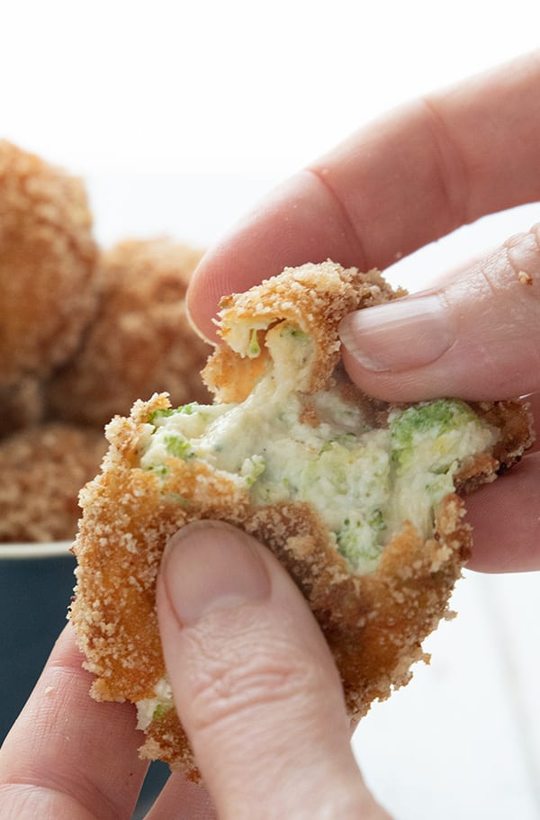 Hands pulling apart fried keto broccoli cheese bites to show the inside.