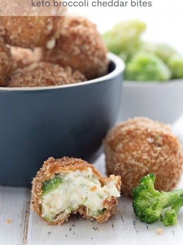 Titled image of keto fried cheese balls on a white table. One is broken open to show the inside, the rest are in a blue bowl.