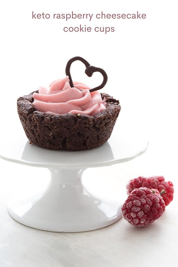 Titled image of a keto chocolate cookie cup filled with raspberry cheesecake on a white cupcake stand.