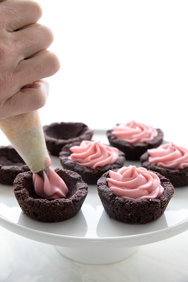 Piping sugar-free raspberry cheesecake into keto chocolate cookie cups