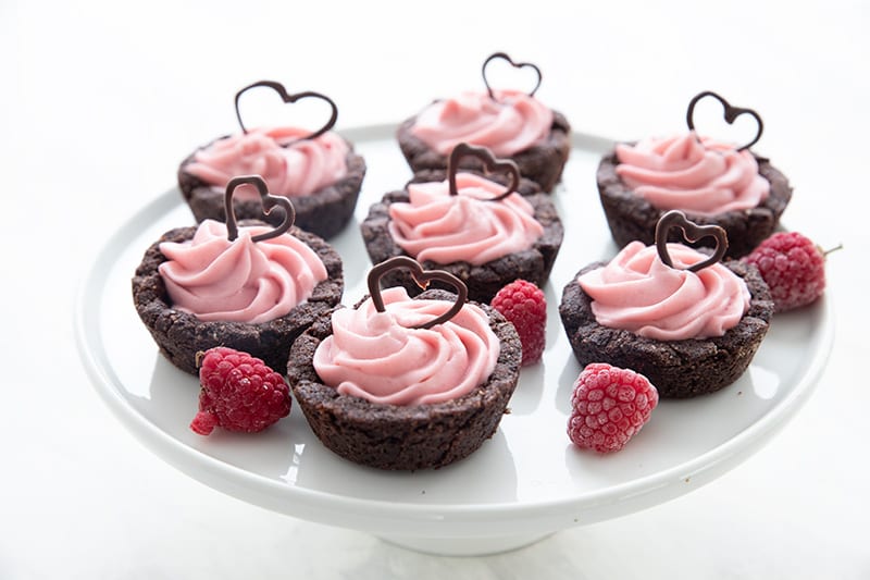 Keto Raspberry Cheesecake Cookie Cups on a white cake stand with raspberries