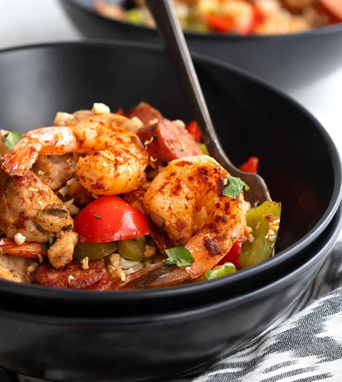 Keto Jambalaya piled up in a black bowl, stacked on top of another black bowls.