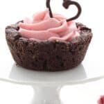 Titled image of a Keto Raspberry Cheesecake Cup on a white cupcake stand with a chocolate heart on top.