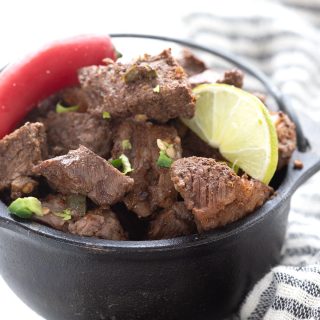 A small cast iron pot filled with keto steak bites, topped with a lime and a chili.