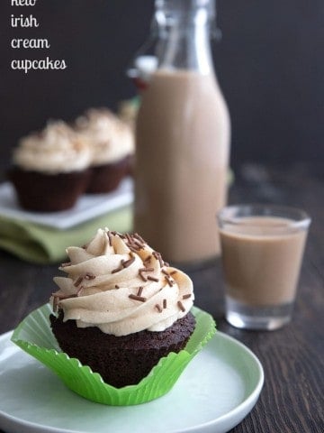 Titled image of a keto Irish Cream cupcake on a white plate, with the bottle of sugar free Irish Cream in behind.