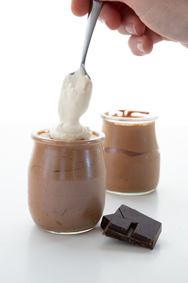 A dollop of whipped cream being added to a jar of keto chocolate mousse