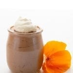A jar of keto chocolate mousse with whipped cream on top beside an orange flower