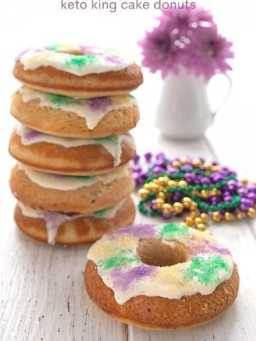 Titled image of king cake donuts with one in front and a stack in behind, on a white table.