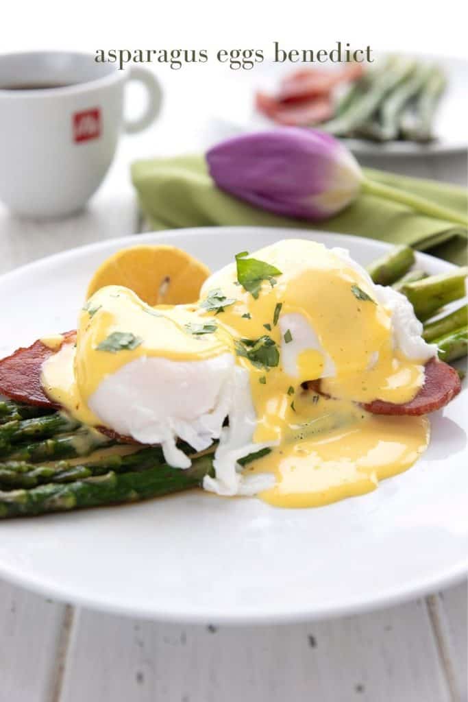 Titled image of eggs benedict served over asparagus on a white plate. A cup of coffee and a purple tulip in the background.