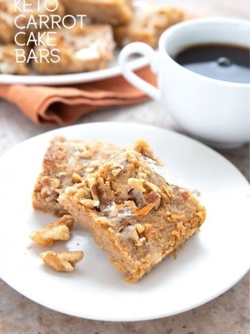Titled image of two keto carrot cake bars on a white plate with a cup of coffee in the background.