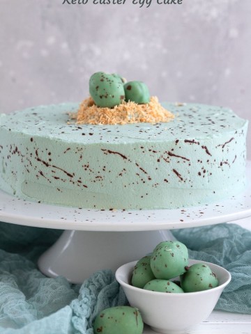 Titled image of a Keto Robin's Egg Cake on a white cake stand, with keto easter eggs on top.
