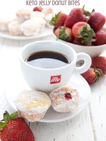 Titled image of keto jelly donut muffins on a saucer with a cup of coffee and strawberries in the background.