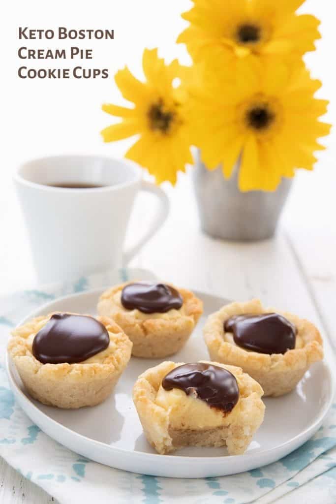 Titled image of Boston Cream Cookie Cups on a white plate over a blue patterned napkin, with a vase of yellow flowers and a cup of coffee in the background.