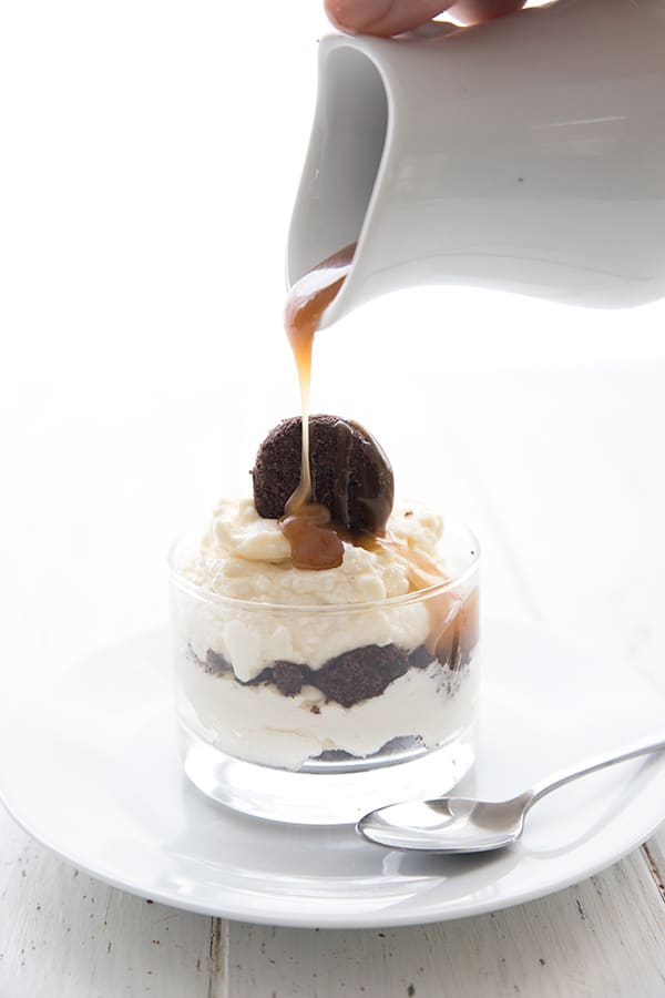 Sugar free caramel sauce being poured out of a white pitcher over a keto brownie parfait