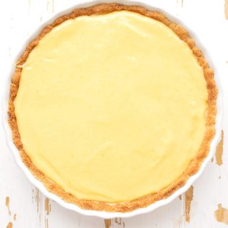 Top down image of keto lemon curd tart in a white ceramic tart pan on a weathered white table.