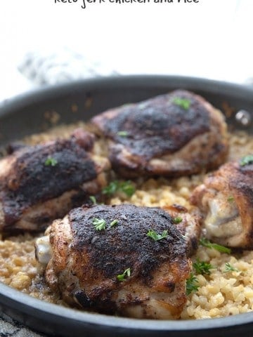 Close up shot of keto jerk chicken and cauliflower rice in a skillet, with parsley sprinkled over top.