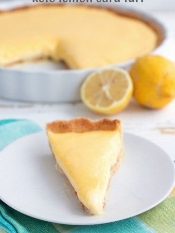 Titled image of keto lemon tart on a white plate with the rest of the tart and some lemons in the background.