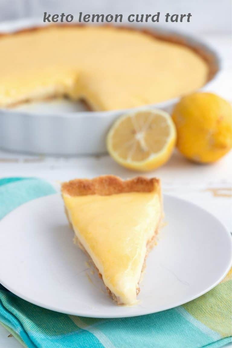 Titled image of keto lemon tart on a white plate with the rest of the tart and some lemons in the background.