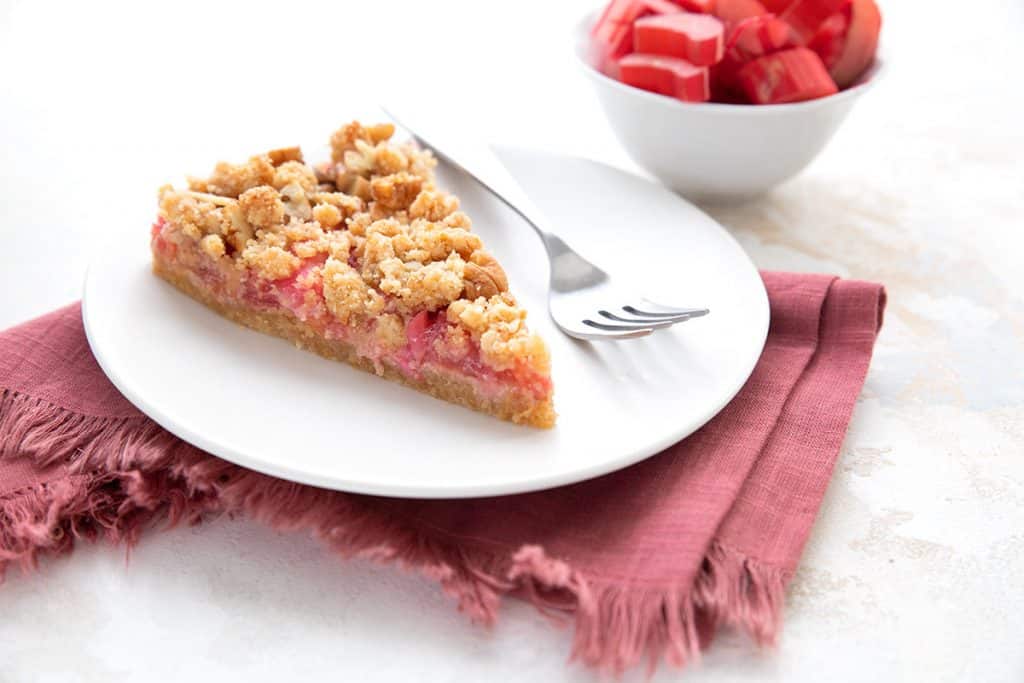 A slice of keto rhubarb tart on a white plate over a red napkin.