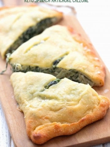 Titled image of a keto spinach artichoke calzone on a cutting board, cut into three pieces.