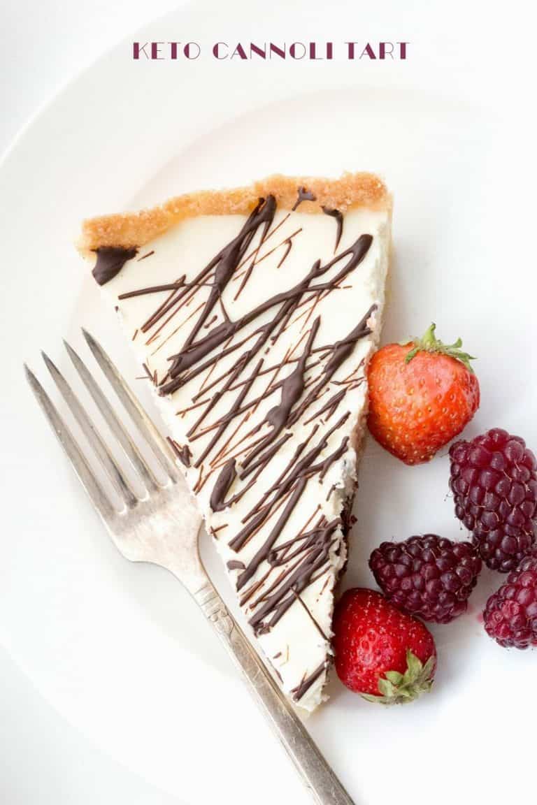 Top down image of a slice of keto cannoli tart with berries on the side, on a white plate.