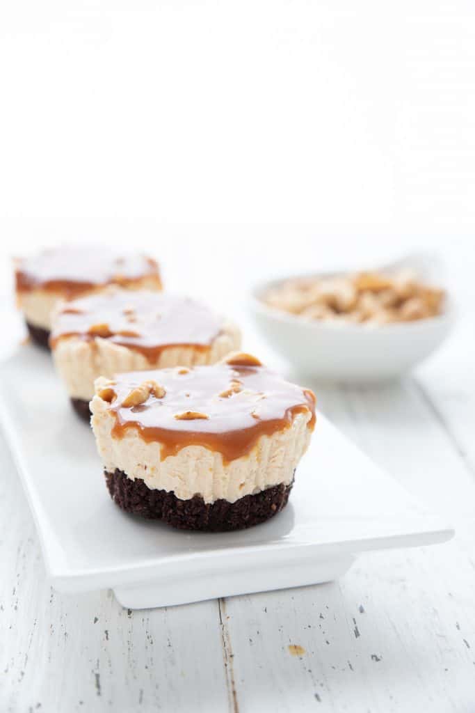 Three mini snickers cheesecakes on a white tray.