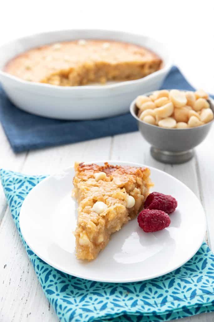 A slice of macadamia nut pie on a white plate with the whole pie in the background.
