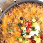 Titled image of a skillet of Keto Mexican Cauliflower Rice on a white table with avocado, tomatoes, and cilantro.