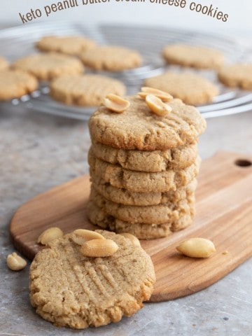 Titled image of a stack of keto peanut butter cookies on a wooden cutting board with peanuts sprinkled around.