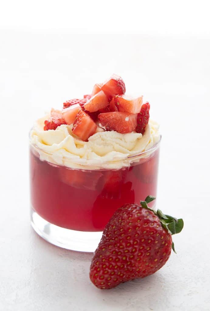 Sugar free strawberry jello in a cup topped with whipped cream and chopped strawberries.
