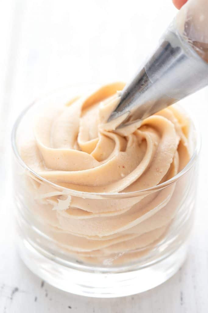 Close up shot of a decorating tip piping keto peanut butter mousse into a dessert cup.